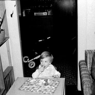 Two children eating cake indoors, one seated at table.