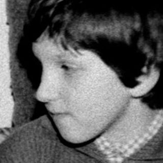 Two children eating cake indoors, one seated at table.
