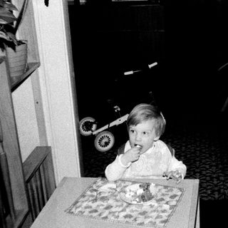 Two children eating cake indoors, one seated at table.
