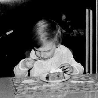 Toddler eating cake at indoor table.