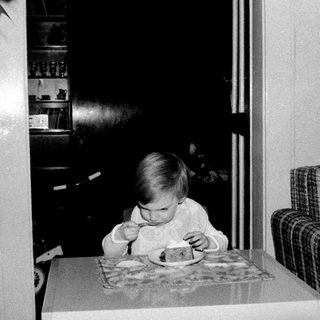 Toddler eating cake at indoor table.