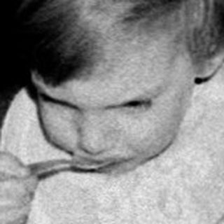 Toddler eating cake at indoor table.