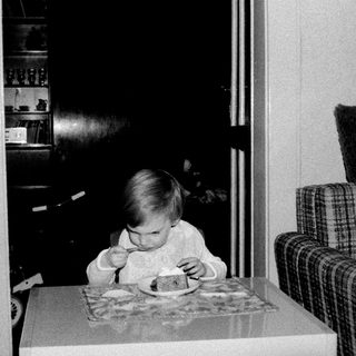 Toddler eating cake at indoor table.