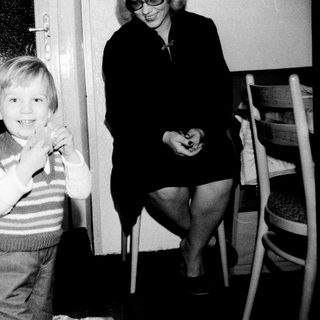 A young boy smiling indoors with a woman.