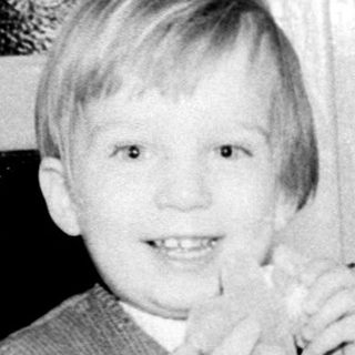 A young boy smiling indoors with a woman.
