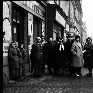Group of people posing outside a building in 1950s-era street scene.