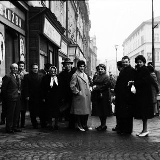 Group of people posing outside a building in 1950s-era street scene.