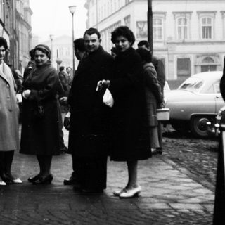 Group of people posing outside a building in 1950s-era street scene.