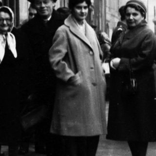 Group of people posing outside a building in 1950s-era street scene.