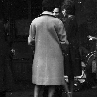 People gathered outdoors in formal attire, possibly at a funeral or memorial.