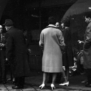 People gathered outdoors in formal attire, possibly at a funeral or memorial.