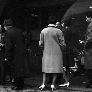 People gathered outdoors in formal attire, possibly at a funeral or memorial.