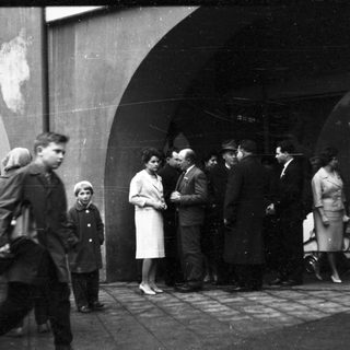 People gathered outdoors near arched entranceway.