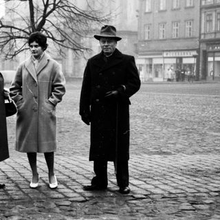 Three people posing outdoors in winter clothing, 1950s-era city square.