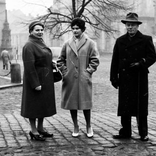 Three people posing outdoors in winter clothing, 1950s-era city square.