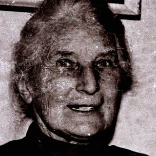 Elderly woman smiling indoors, mid-20th century.