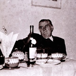 Old man toasting at a formal dinner table.