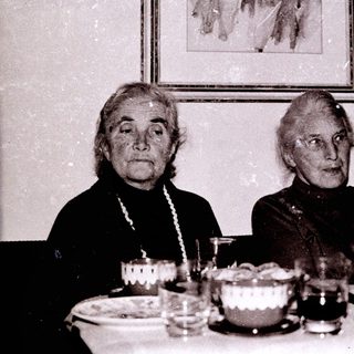 Two elderly women seated indoors at a table.