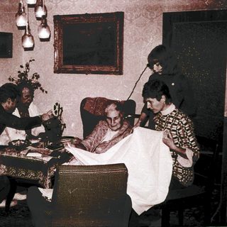 Family gathering around elderly woman receiving haircut.