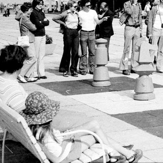 People playing giant outdoor chess on a large board.