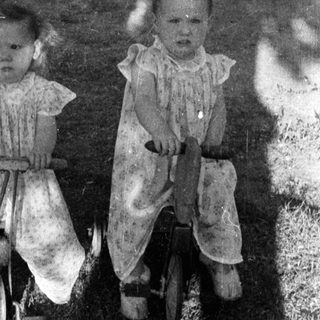 Two young children riding a tandem bicycle outdoors.