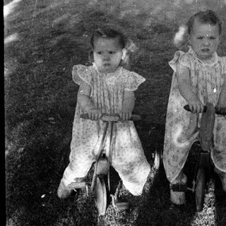 Two young children riding a tandem bicycle outdoors.