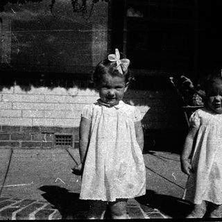 Two young girls in vintage dresses, posing outdoors.