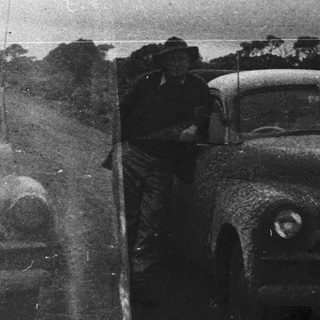 Two vintage cars with people standing outside.