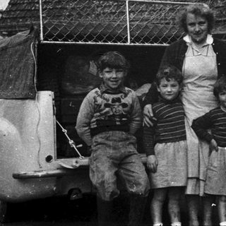 Family posing outside vintage house with old car.