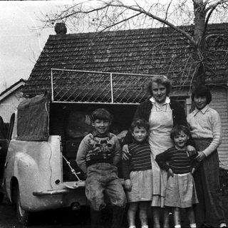 Family posing outside vintage house with old car.