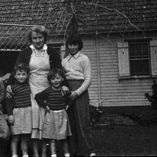 Family posing outside vintage house with old car.