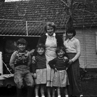 Family posing outside vintage house with old car.