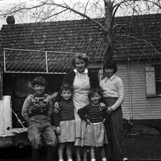 Family posing outside vintage house with old car.