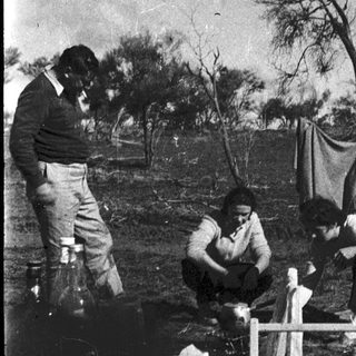 People tending to a small fire outdoors in rural setting.