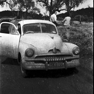 Classic car with vintage license plate, two men working on hood outdoors.