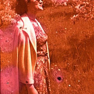 Vintage photo of woman smiling outdoors in floral dress.
