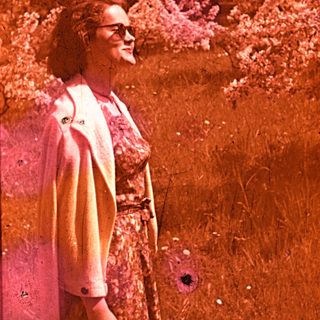 Vintage photo of woman smiling outdoors in floral dress.