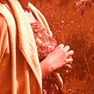 Woman in vintage clothing standing outdoors in sunlight.