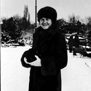 Smiling woman in winter coat and fur hat outdoors.