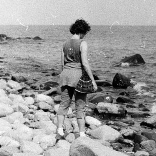Two people walking along rocky seaside shore.