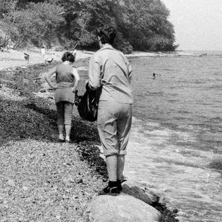 People walking along a rocky riverside shore.