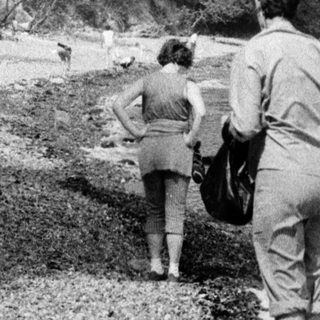 People walking along a rocky riverside shore.