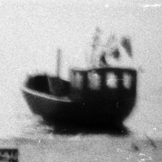Miniature scene of beach with toy boat, cart, and box.