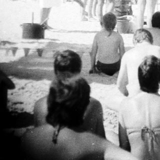 Group of people watching beachside performance or ceremony.