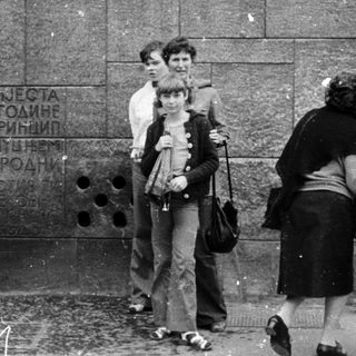 People waiting at a monument plaque on rainy day.