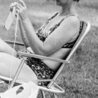 Woman knitting outdoors on a chair.