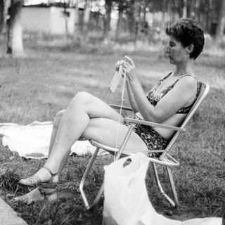 Woman knitting outdoors on a chair.