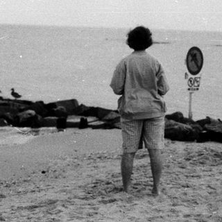 Person standing by ocean waves near pier.