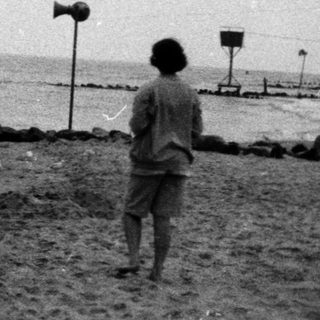 Person walking alone on beach near ocean waves.