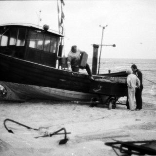 Old fishing boat on shore with three people.